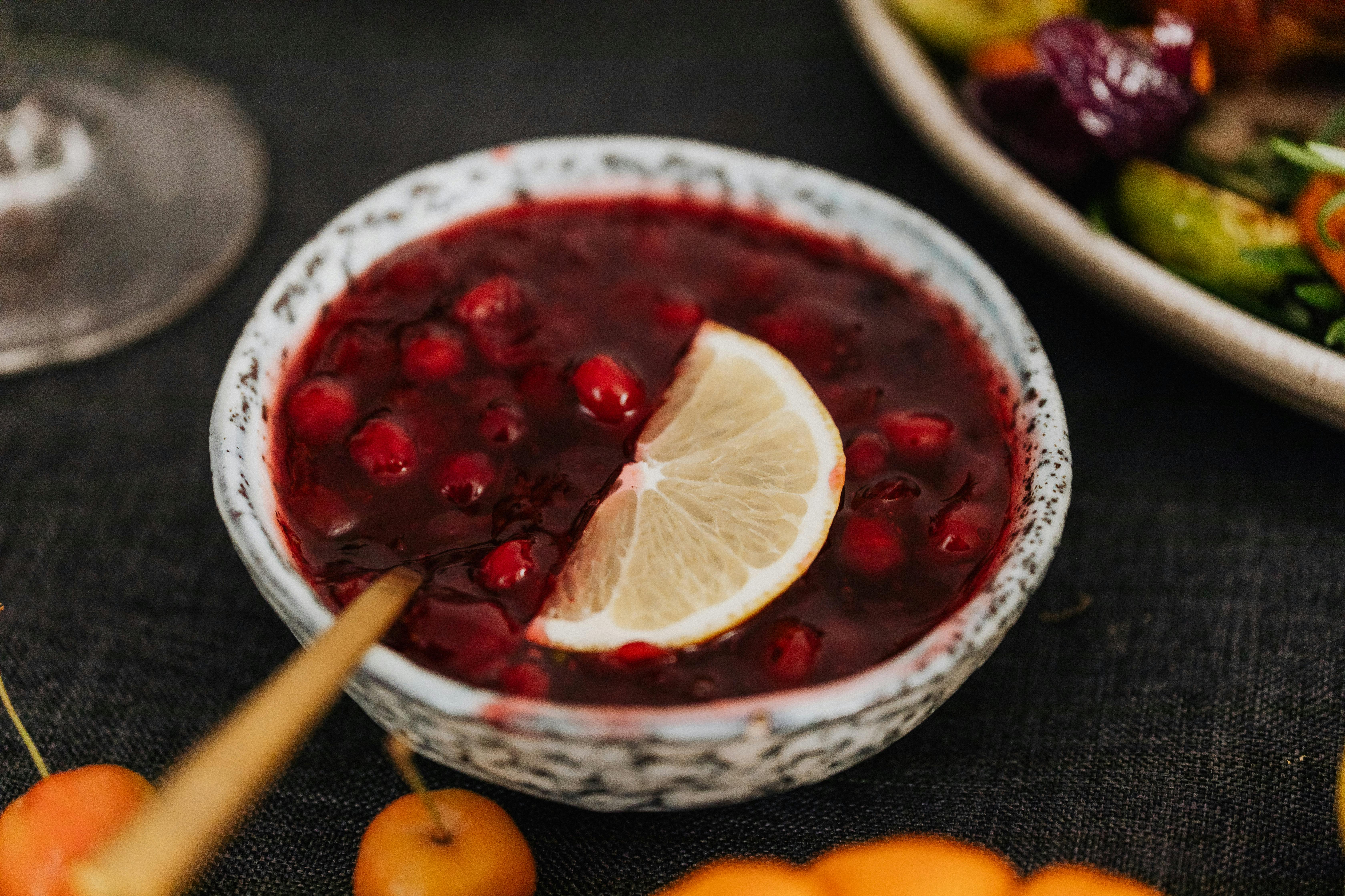 Close-up of a delicious cranberry sauce garnished with a lemon slice in an artistic ceramic bowl.