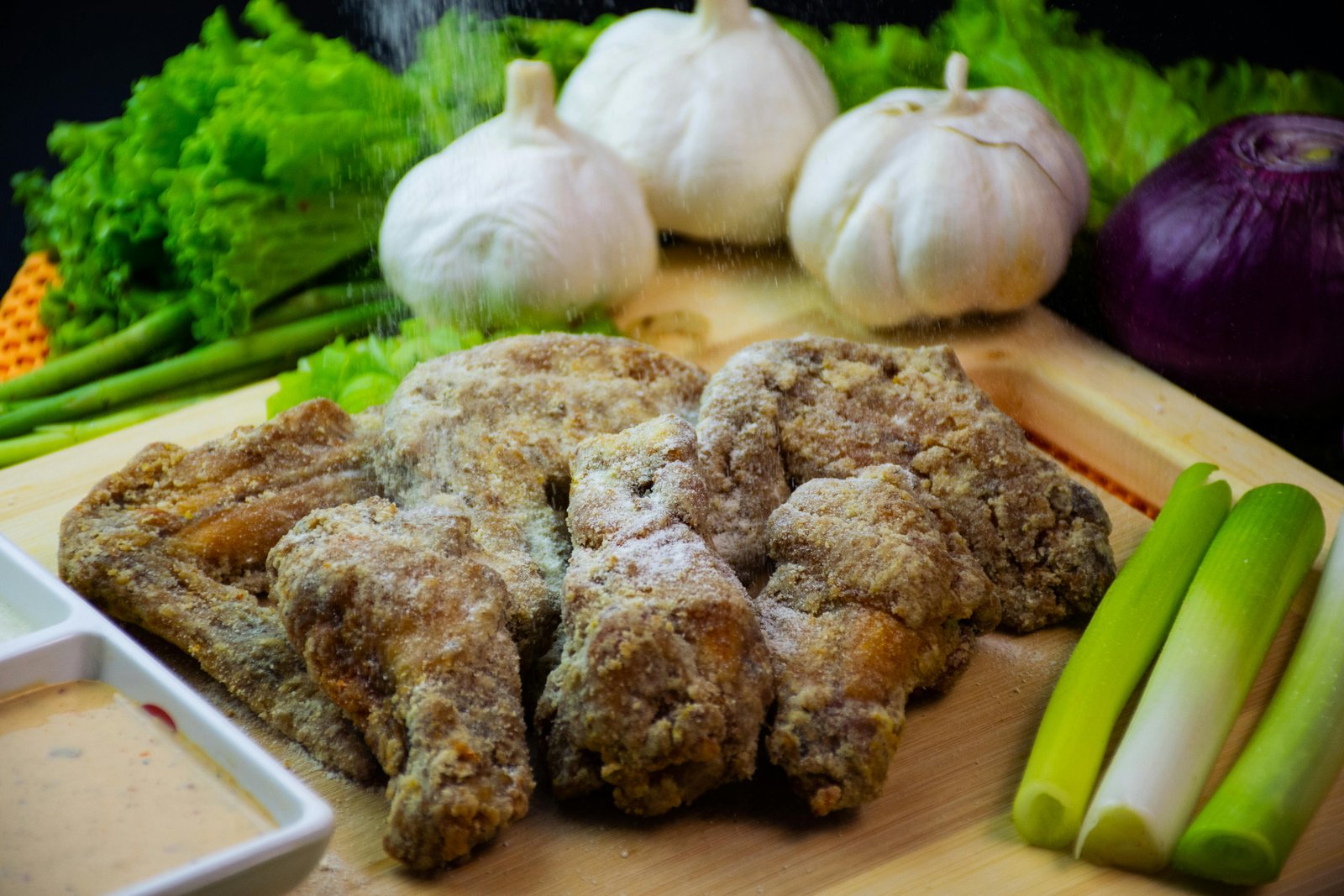 Close-up of seasoned chicken wings with fresh garlic, onions, and greens on a wooden board.