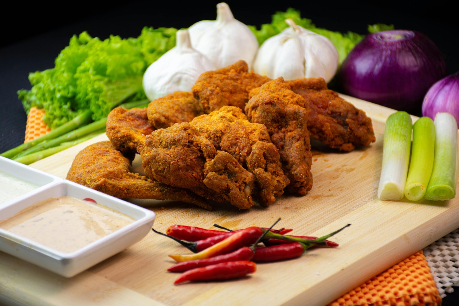 Close-up of spicy fried chicken with fresh vegetables and dipping sauce on a wooden board.