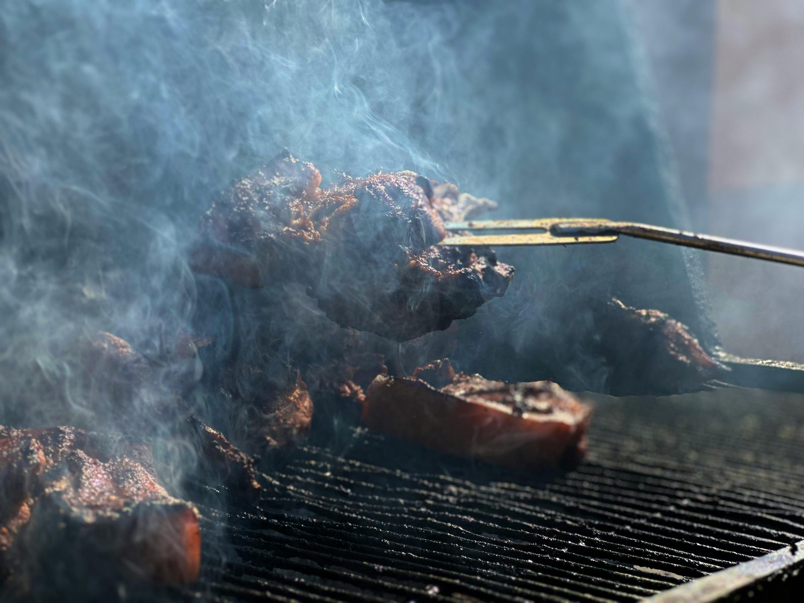 Close-up of meat sizzling on a smoky barbecue grill outdoors.