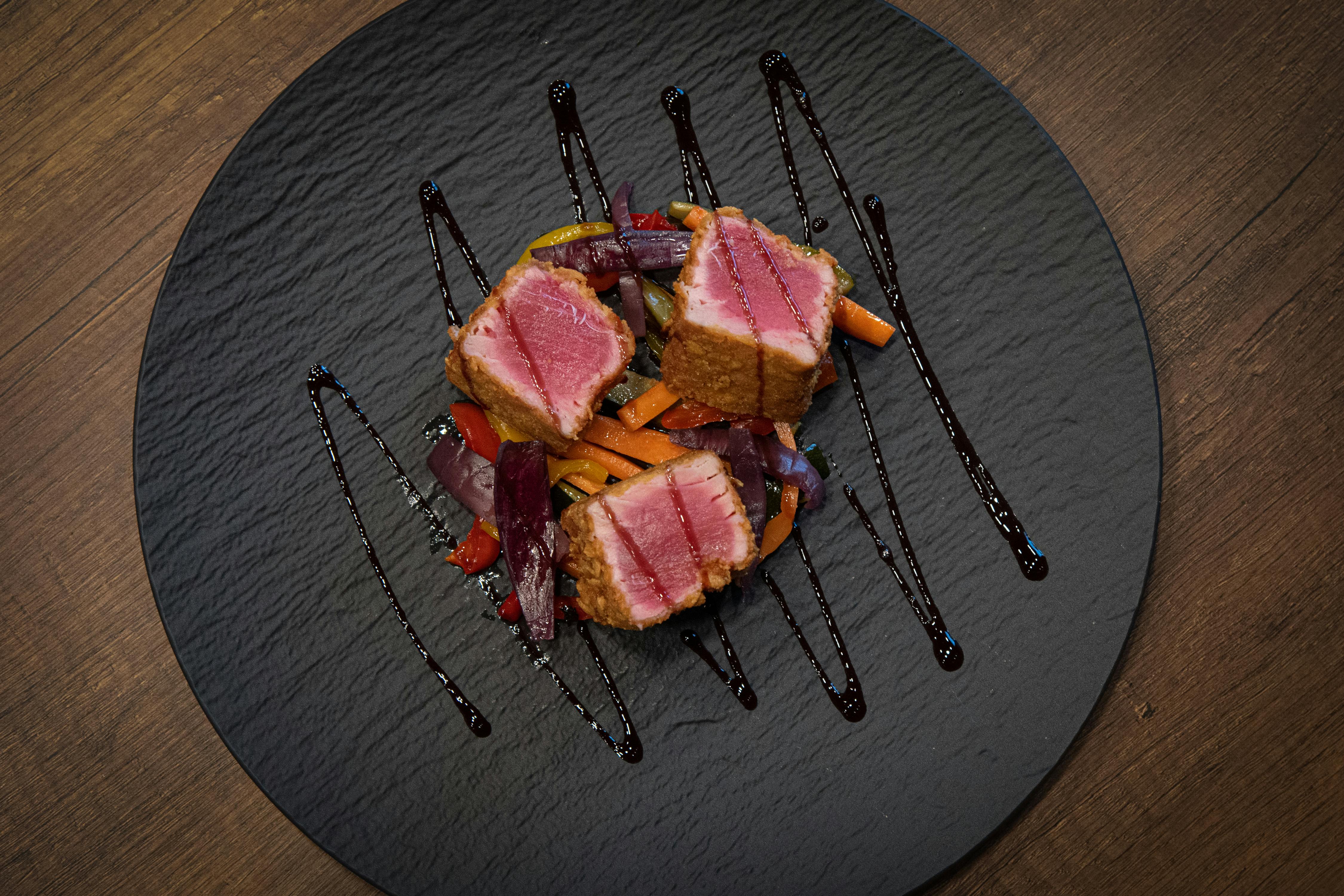 Savor gourmet ahi tuna steak with colorful glazed vegetables on an elegant black plate.