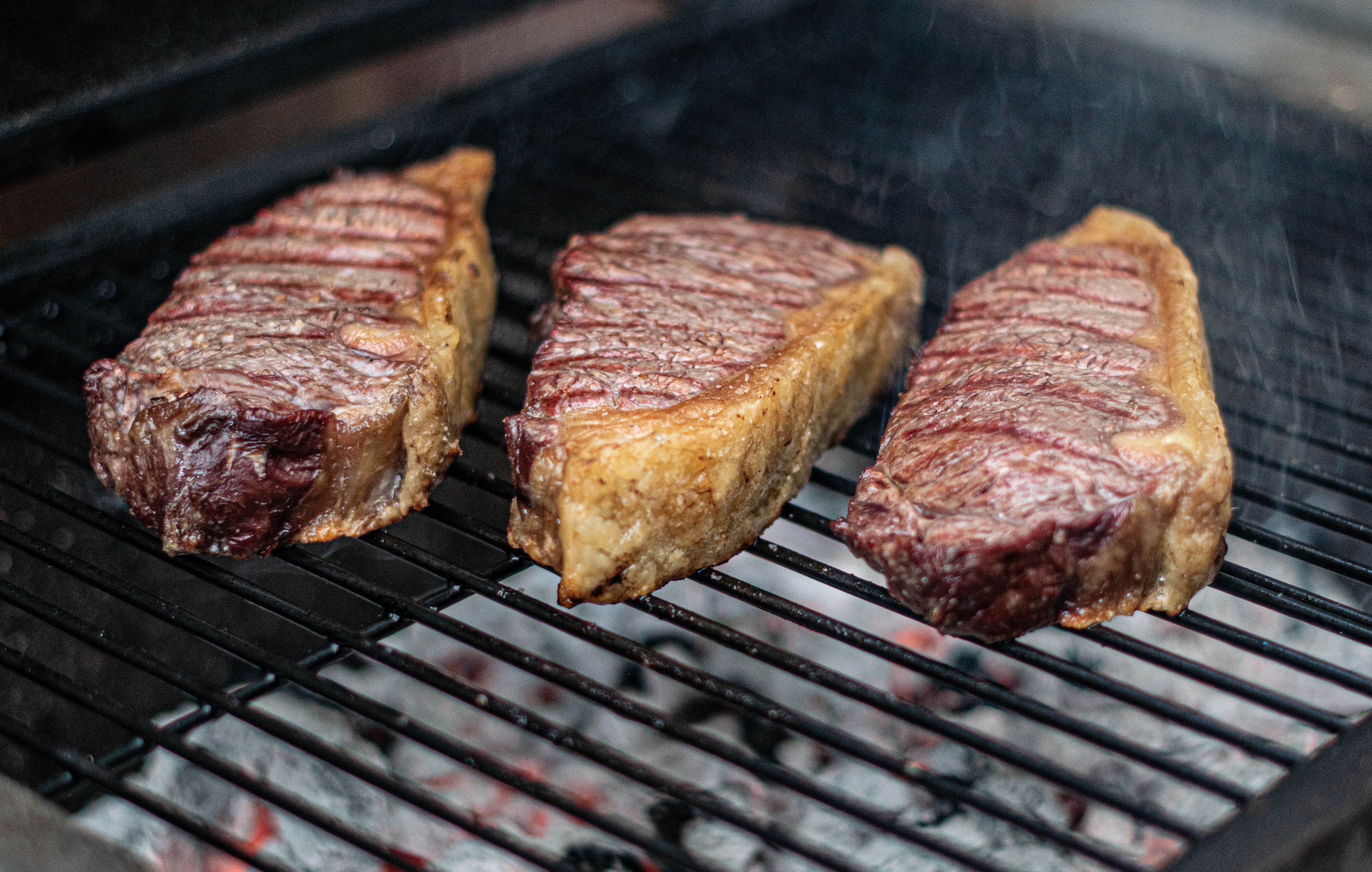 Close-up of three juicy steaks grilling on a barbecue, perfect for a summer cookout.