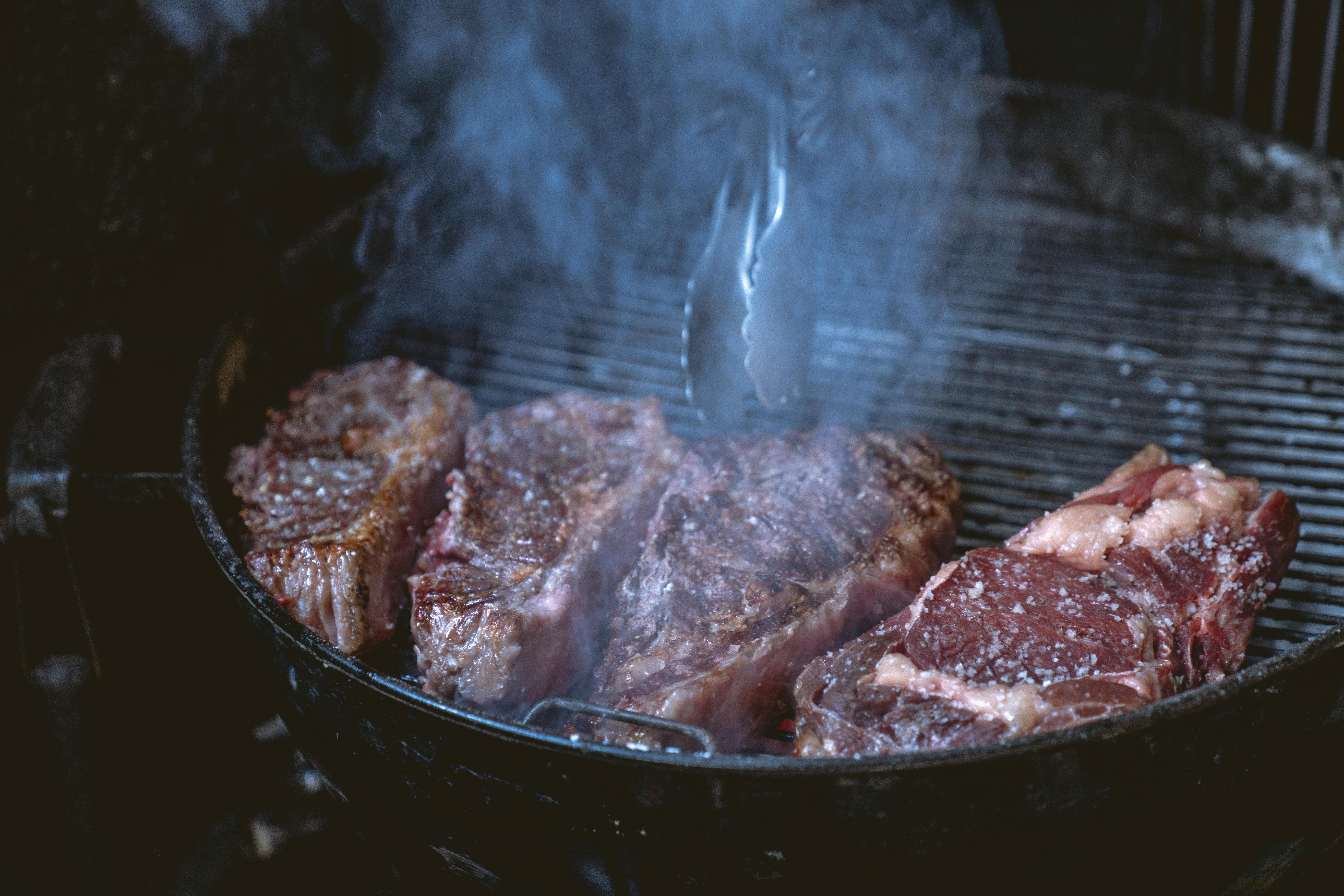 Close-up of juicy steaks sizzling on a smoky barbecue grill, ideal for a food or lifestyle theme.